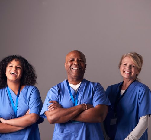 Studio Portrait Of Three Members Of Surgical Team Wearing Scrubs Standing Against Grey Background Studio Portrait Of Three Members Of Surgical Team Wearing Scrubs Standing Against Grey Background